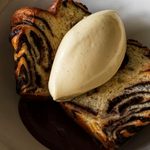 Slice of marbled chocolate cake topped with a scoop of creamy vanilla ice cream on a white plate, creating a rich and indulgent dessert scene.