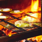Grilled seafood on a wire rack over an open flame. Scallops are being cooked, glowing warmly, with flames highlighting the vibrant orange and red hues.