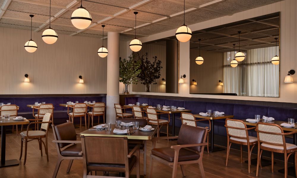 Stylish restaurant interior with modern decor, featuring round pendant lights, wooden tables, padded chairs, and a large mirror reflecting the cozy ambiance.